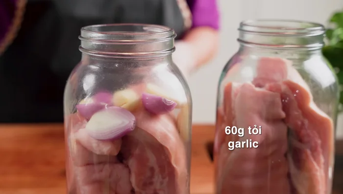 Layer the jars: Place pork belly pieces, shallots, garlic, bay leaves, and peppercorns into each jar.