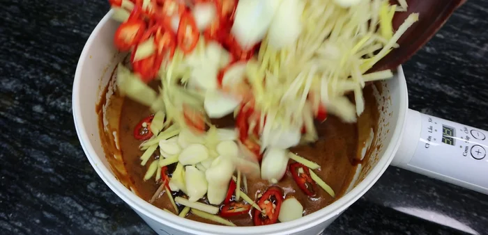 Once cool, add the sliced garlic, chili, ginger, and galangal to the sugar-fish sauce mixture and mix well.