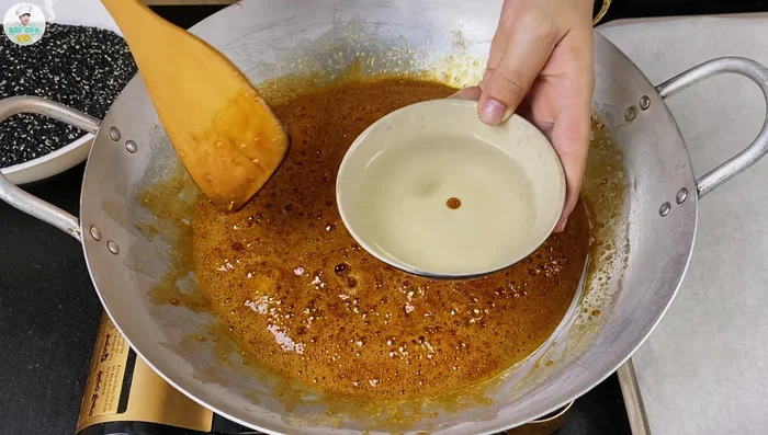 Once the syrup reaches the correct consistency, add the roasted sesame seeds and peanuts. Stir until well combined and the mixture is evenly coated.