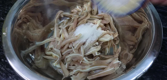 Place sliced pig ears in a basin. Add sugar, salt, and ice. Squeeze the pig ears to remove excess fat and make the water clear. (186.239)