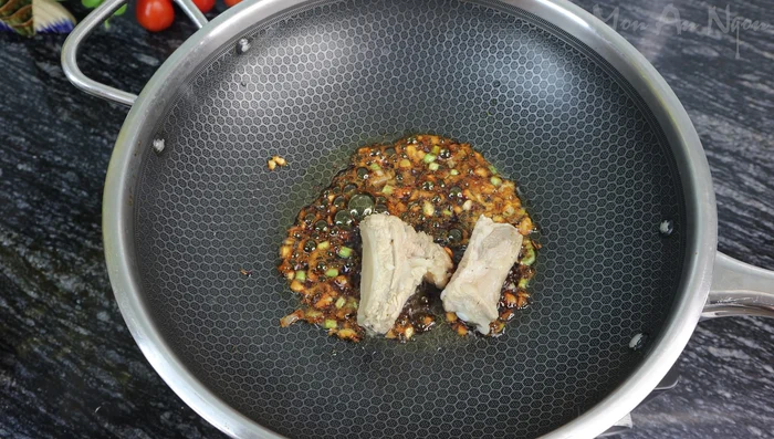 Add ribs and aromatics: Add the marinated ribs to the caramelized sugar, followed by the garlic and onion roots. Stir well to coat the ribs evenly.