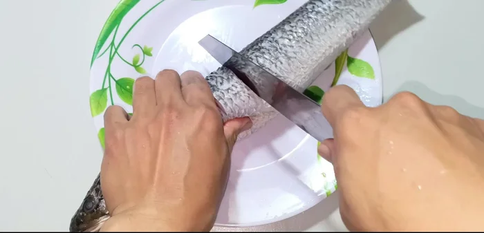 Lightly score the fish's body with a knife, being careful not to cut too deep into the bones. This helps the fish cook evenly and absorb the sauce better.