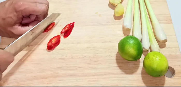 Prepare the aromatics: slice chili peppers, lemongrass, and ginger. Cut lemon leaves in half.