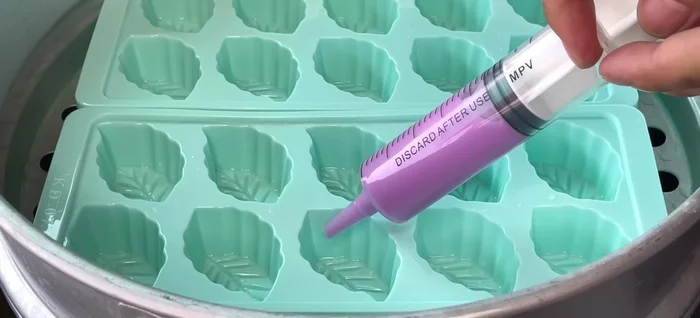 Pour the batter. Pour a small amount of each colored batter into the molds, creating a leaf design. Start with one end, leaving the center for the mung bean filling. Steam for 2 minutes over low heat. Add a layer of mung bean filling halfway up the mold. Steam for 5 minutes over medium heat. Add a final layer of batter (half purple, half pandan). Steam for 6 minutes over medium heat.