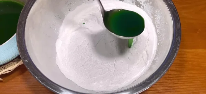 Gradually add the colored coconut milk to the roasted flour, mixing slowly until the mixture is evenly moist and loose. If too dry, add more liquid.