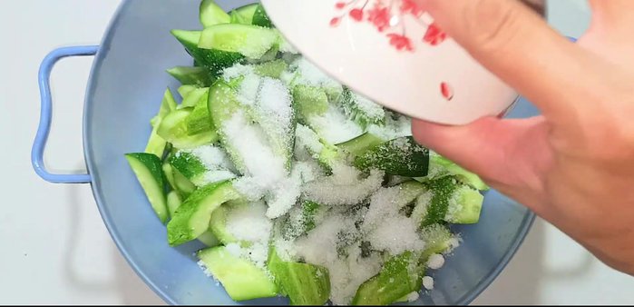 In a bowl, mix 80g of sugar (or salt), sliced garlic, and chopped chilies with the cucumbers. Let it sit for 2 hours to release water and soften.