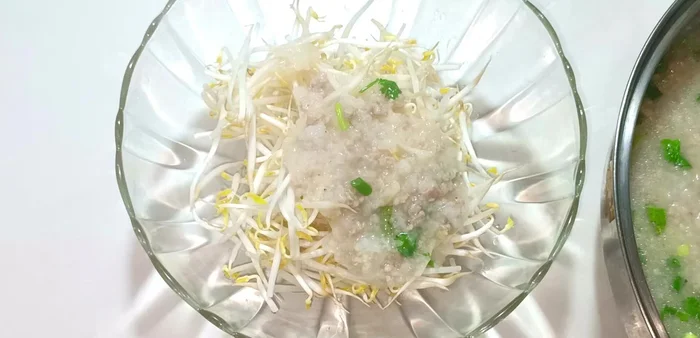 Serve the porridge over bean sprouts in a bowl. Garnish with green onions, cilantro, fried onions, and ground pepper. Add a squeeze of lemon juice before eating.