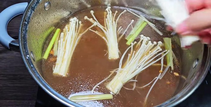 Add enoki mushrooms, Vietnamese coriander, and cilantro to the hot pot broth.