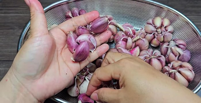 Peel and thinly slice 500g of purple garlic. (Note: The narrator mentions that purple garlic is harder to peel and suggests tips on buying larger bulbs for faster peeling.)