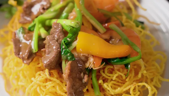 Assemble and serve: Layer crispy noodles, stir-fried vegetables, shrimp, squid, and beef on a plate. Drizzle with sauce and garnish with green onions and pepper.
