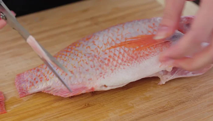 Prepare the fish (red tilapia). Clean the fish thoroughly, removing scales, intestines, blood, fins, and tail. Make three light cuts at a 45-degree angle to create larger scales for better marinade absorption.