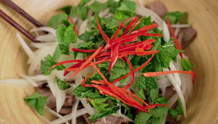 Combine the blanched beef, onions, herbs, and chili peppers in a bowl. Drizzle with additional salad dressing, and mix gently.