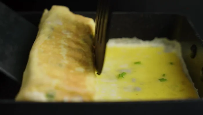 Continue adding egg mixture and rolling to create a thick omelet roll. Fry until desired thickness is reached. Cut the rolled omelet into small rectangular pieces.