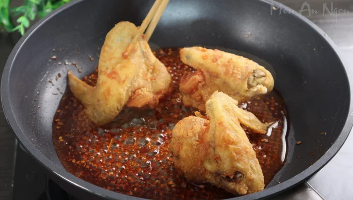 Add the fried chicken wings to the sauce, mixing well to coat them evenly. Add the fried garlic and chili, mixing gently.