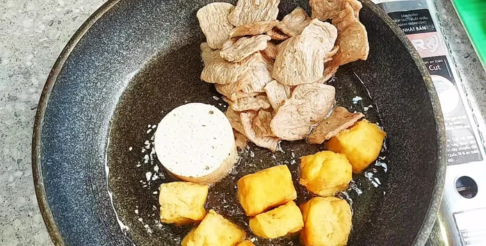 While the broth simmers, fry the tofu until golden brown. Fry the vegetarian chicken and beef patties, then slice them thinly for garnish.
