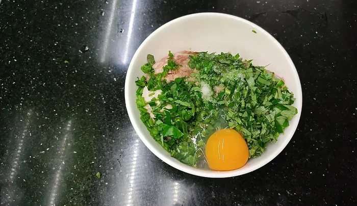 Add an egg, finely chopped green onions, and lolot leaves to the marinated meat. Mix well.