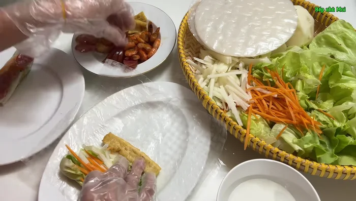Assemble the spring rolls: Lay out rice paper, add desired fillings (shrimp, tofu, Chinese sausage, peanuts, vegetables, cassava), and roll tightly.