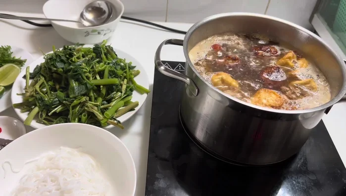 Blanch vermicelli noodles in boiling water. Prepare your garnishes: bean sprouts, shredded water spinach, perilla, and Vietnamese coriander.