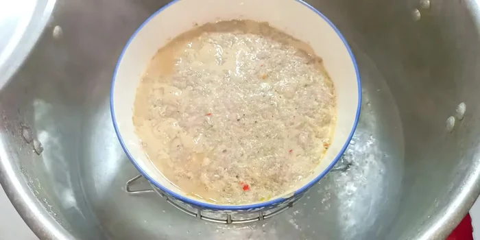 After 20 minutes of steaming, briefly open the lid to allow excess water to drip off, then pour the whisked egg evenly over the meat.