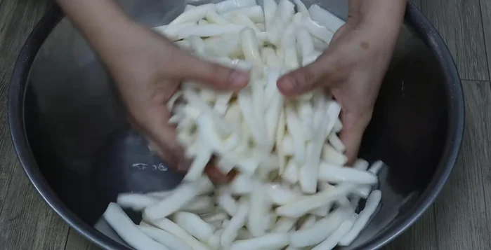 The next morning, drain the excess water from the salted radish. Use a cloth bag or towel and squeeze out as much water as possible to speed up the drying process.