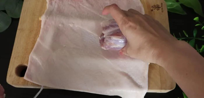 Place the pork leg on top of the skin, and roll it up tightly, using the chopsticks to help shape it. Tie the roll securely with the strings.