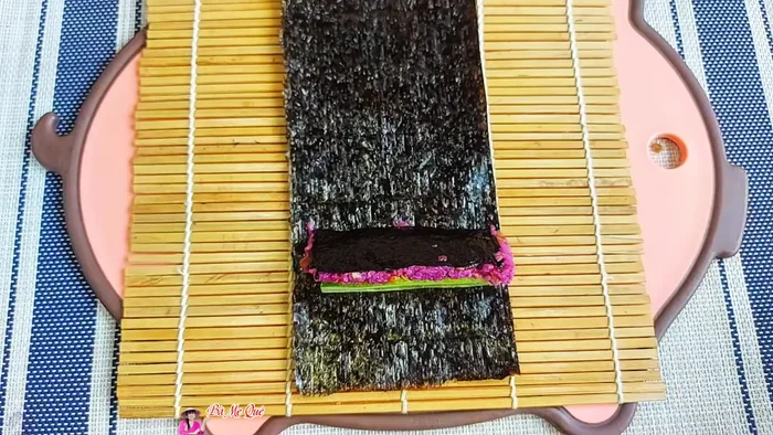 Prepare another sheet of seaweed. Place each cucumber slice and a carrot stick in one corner. Place the rolled rice in the center. Add the remaining rice and roll again into a square shape.