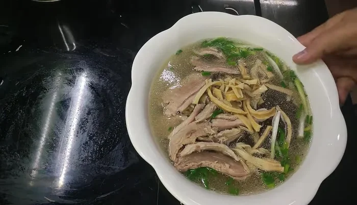 Pour the goose broth over the noodles and duck.