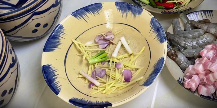 Layer the ingredients in a bowl: Start with ginger, shallots, and green onion roots at the bottom. Add a layer of pork belly, followed by mackerel fish sauce (discarding the oil), and shrimp. Repeat layers.