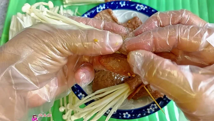 Take a slice of vegetarian beef, place enoki mushrooms inside, roll tightly, and secure with a bamboo stick.